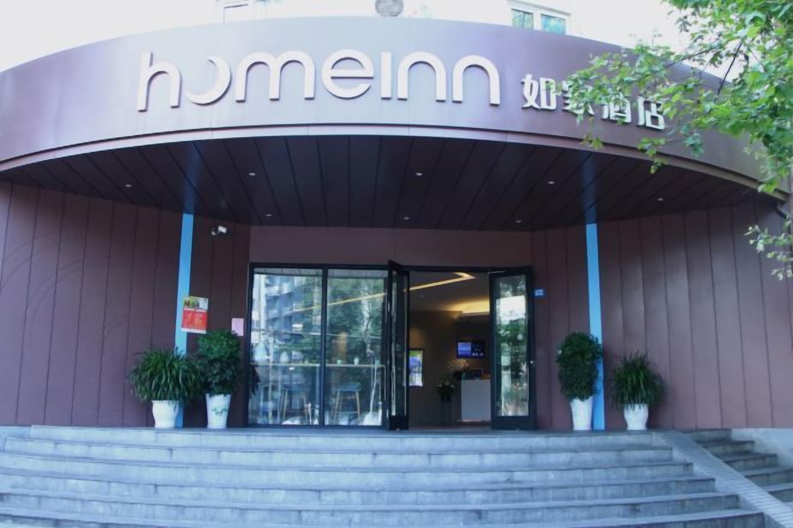 The exterior of a hotel with a curved entrance, a sign with the name 'homeinn,' and potted plants on the steps.