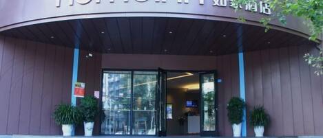 The exterior of a hotel with a curved entrance, a sign with the name 'homeinn,' and potted plants on the steps.