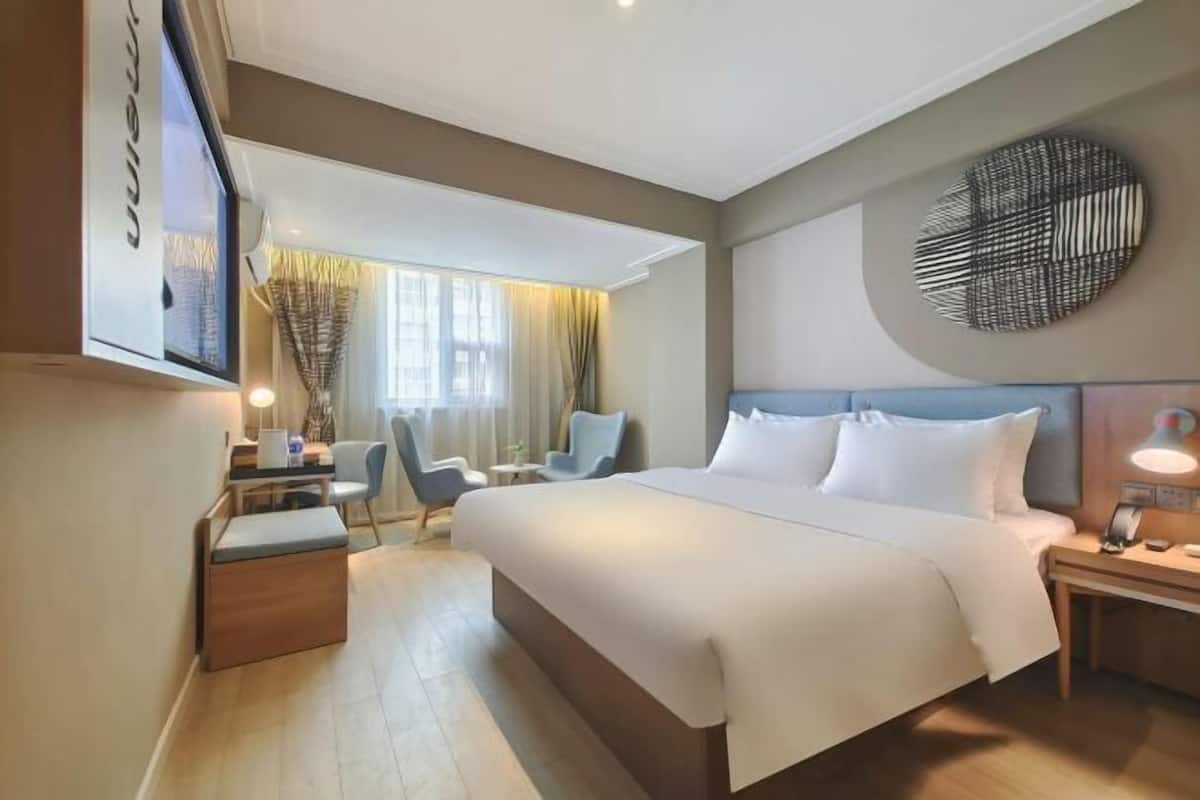 A hotel room with a large bed, a desk with a chair, a small table, and a TV mounted on the wall.