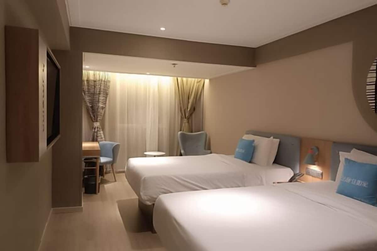 A hotel room with two beds, a desk, a chair, and a TV.