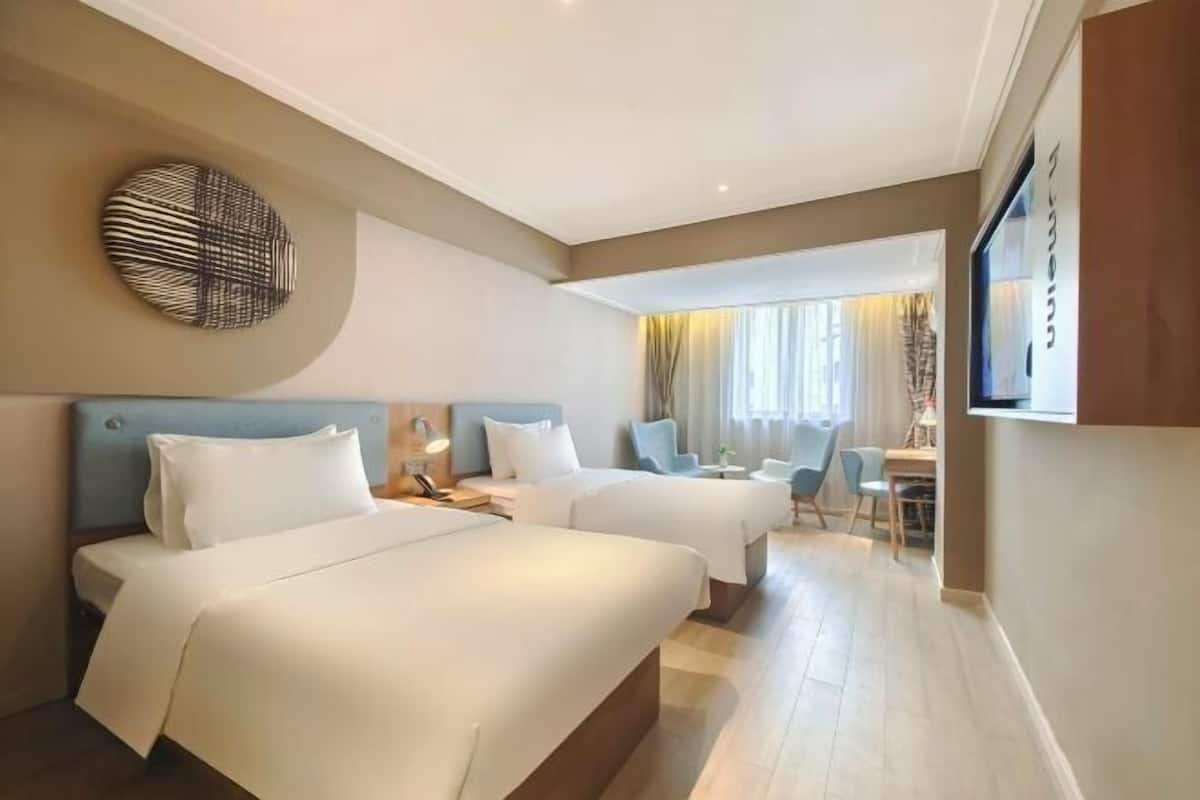 A hotel room with two beds, a desk, a chair, and a large window.