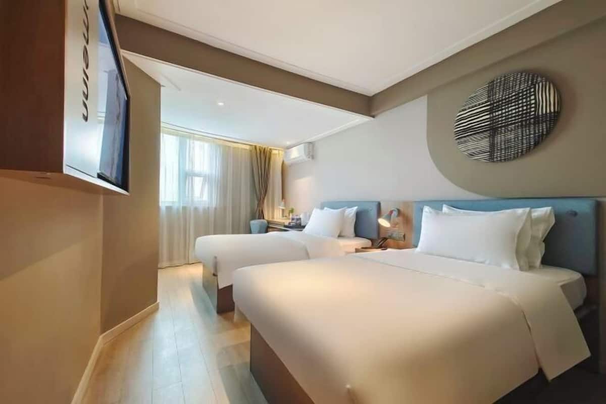 A hotel room with two beds, a TV, a round wall decoration, and a window with curtains.