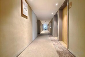 A long, narrow hotel corridor with framed artwork on the walls and a carpeted floor.