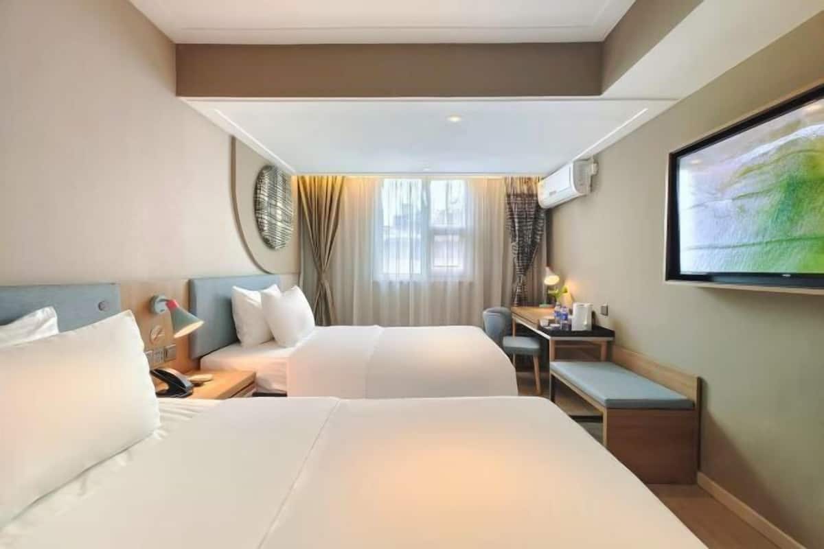 A hotel room with two beds, a desk, a chair, a TV, and a window with curtains.