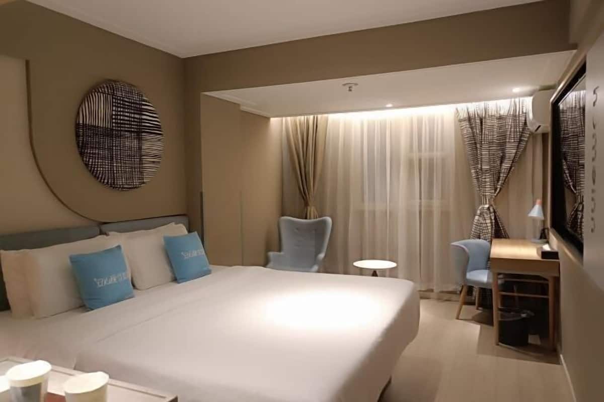 A hotel room with a large bed, a desk, a chair, a round wall decoration, and curtains.