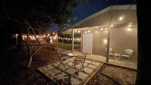 Eine Terrassenfläche im Freien mit Tisch, Stühlen, einer Tür und Lichterketten.