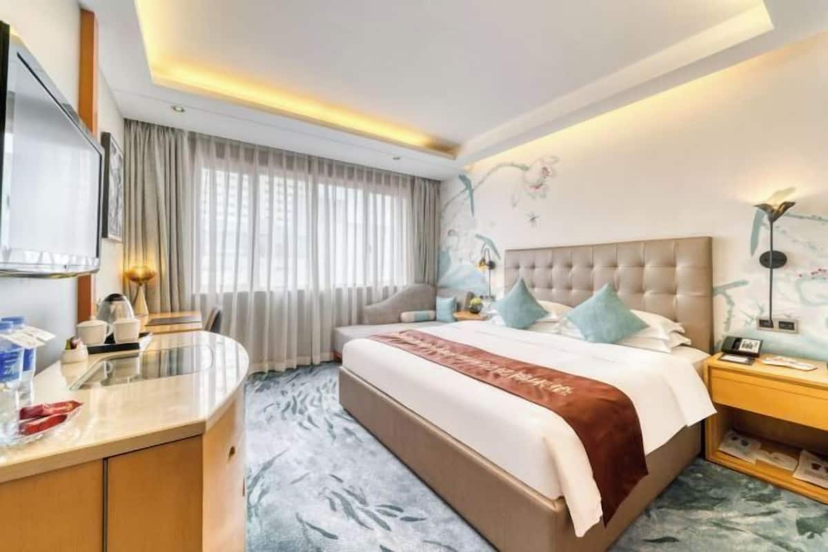 Una habitación de hotel con una cama grande, un escritorio, una silla, una mesita de noche y un televisor.