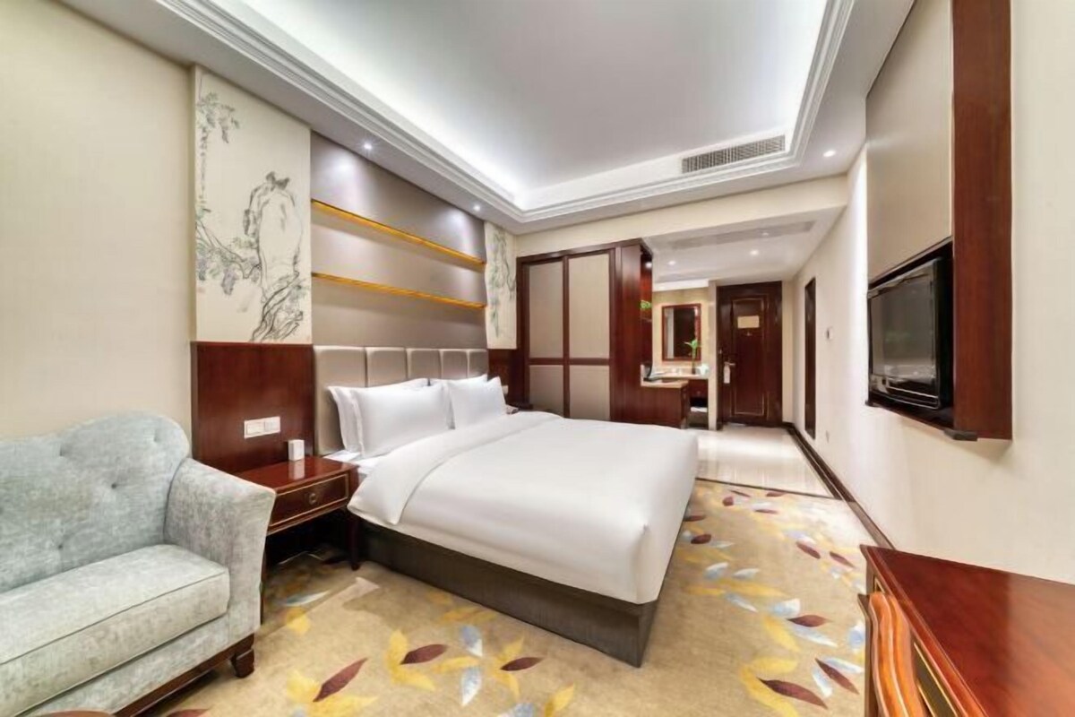 A hotel room with a large bed, a sofa, a desk, and a TV.
