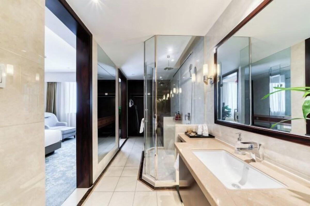 A modern bathroom with a large mirror, a glass shower enclosure, and a beige countertop.