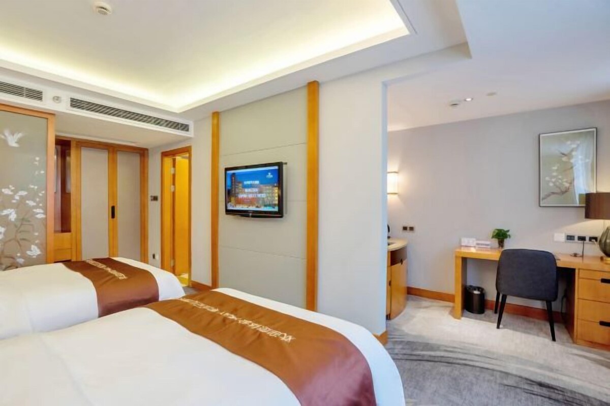 A hotel room with two beds, a desk, a chair, a television, and a framed picture on the wall.