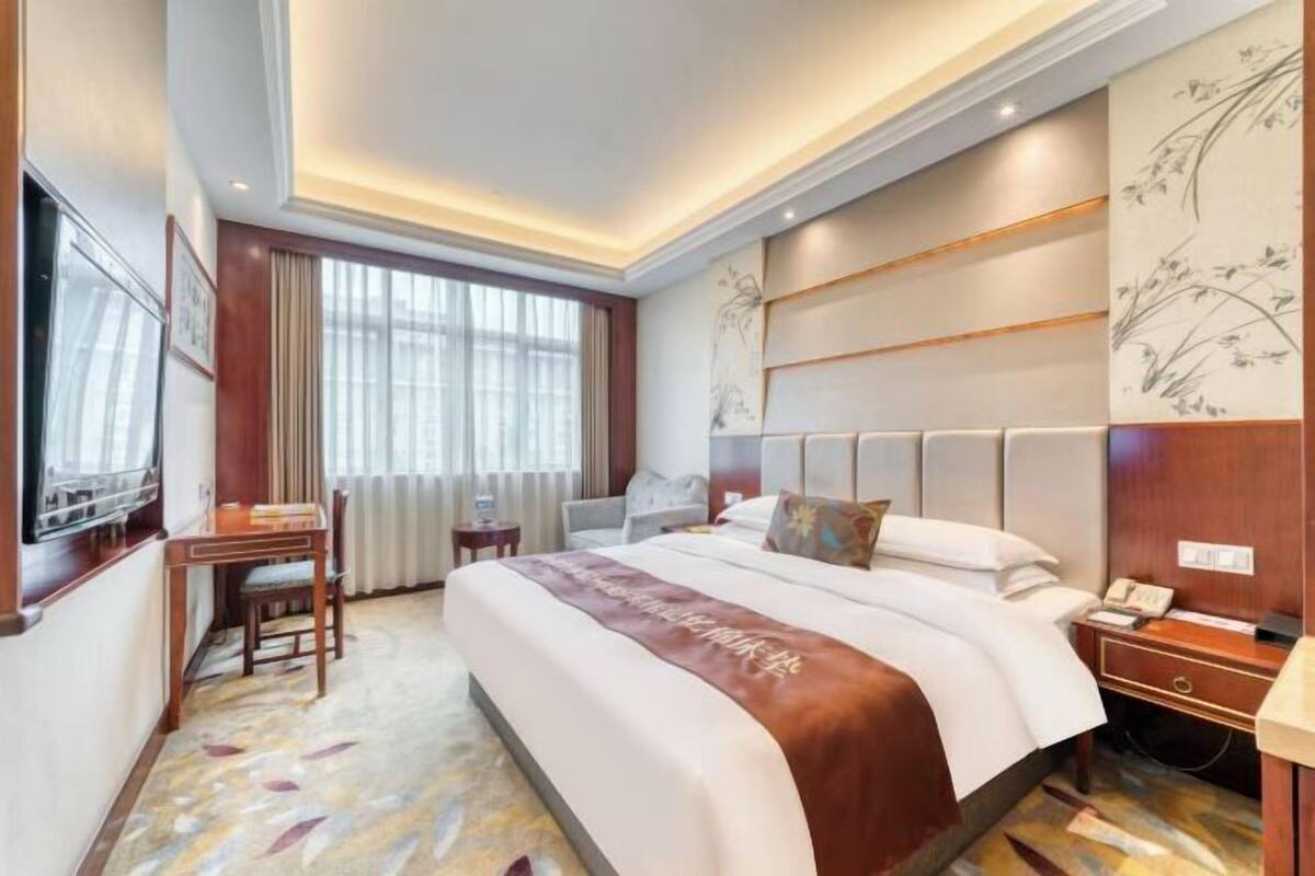 Habitación de hotel con una cama grande, un escritorio, una silla, un televisor y una ventana con cortinas.