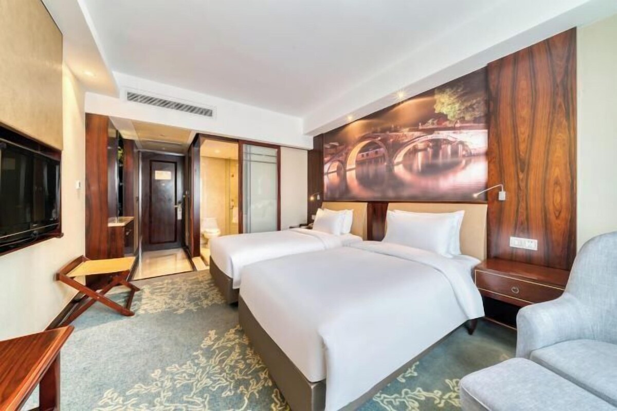 A hotel room with two beds, a TV, a desk, and a chair.