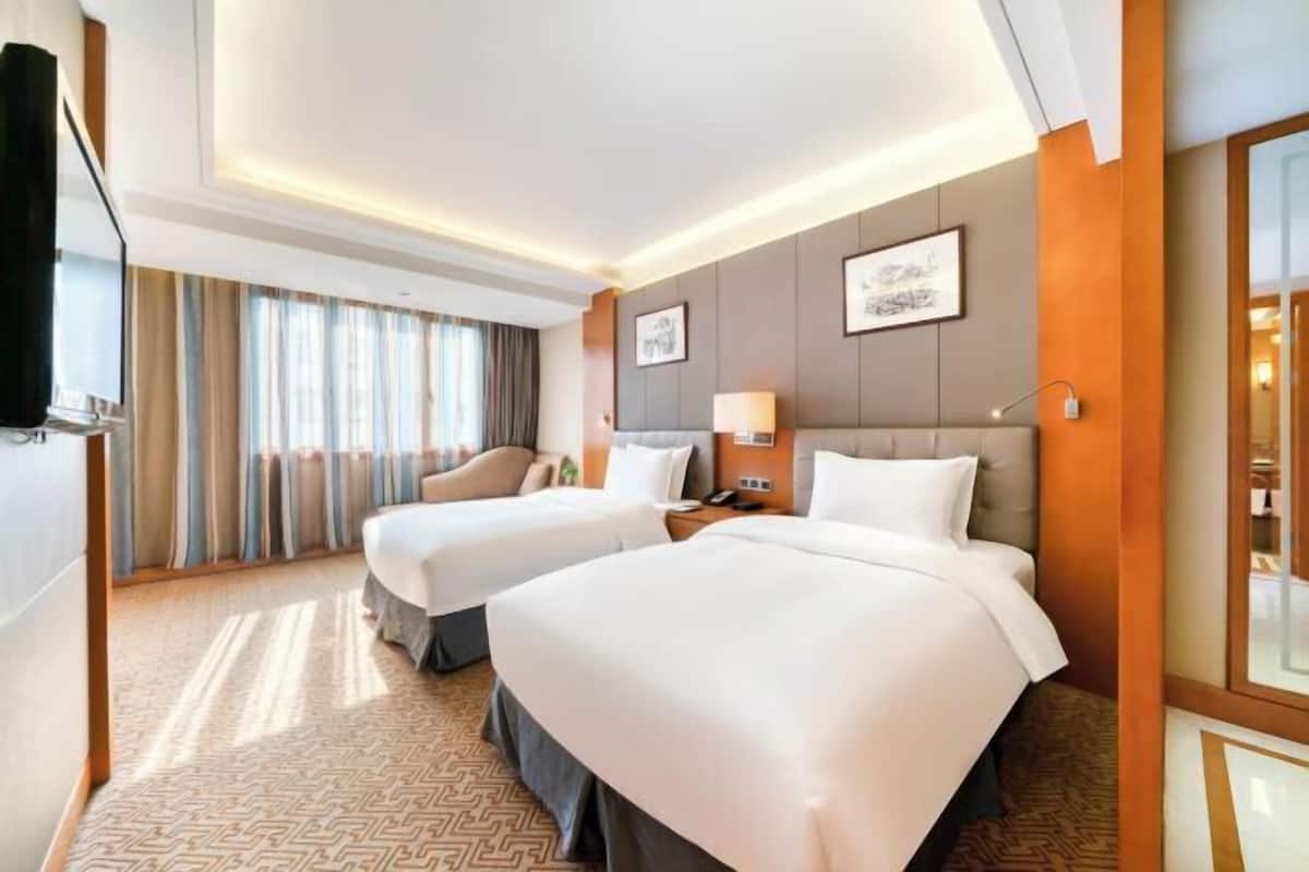 Habitación de hotel con dos camas, un sofá, un televisor y un ventanal con cortinas.