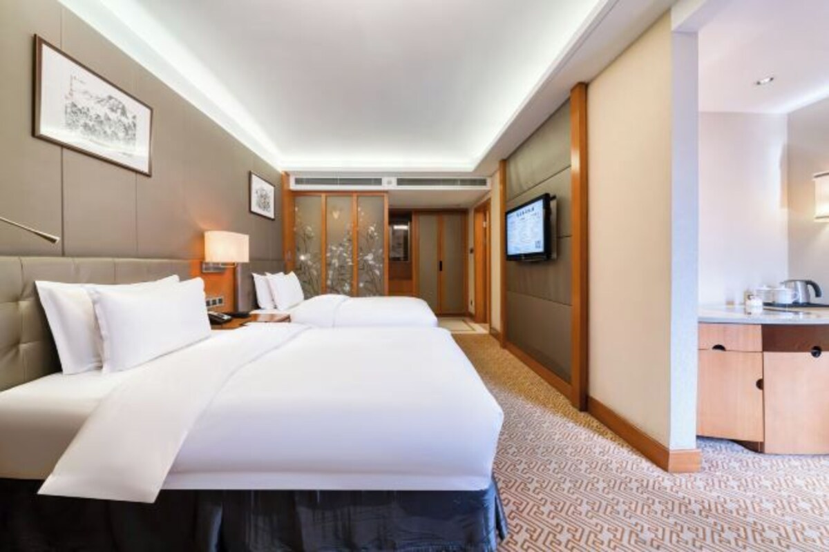 A hotel room with a large bed, a desk with a chair, a TV, and a bathroom with a sink and mirror.