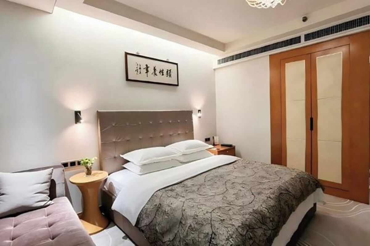A hotel room with a bed, bedside tables, a nightstand, a wardrobe, and a wall-mounted artwork.