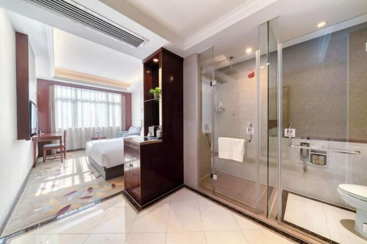 Habitación de hotel con cama, escritorio, silla, ducha e inodoro.