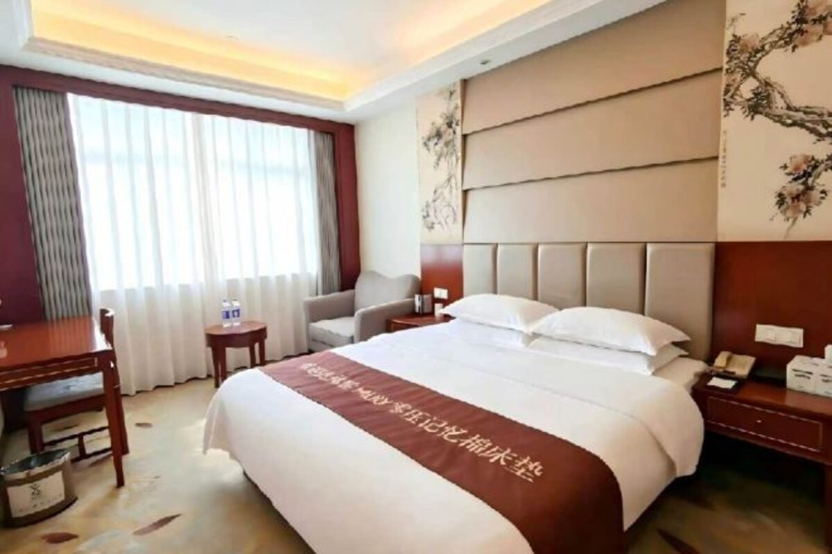 A hotel room with a large bed, a desk, a chair, and a small table.