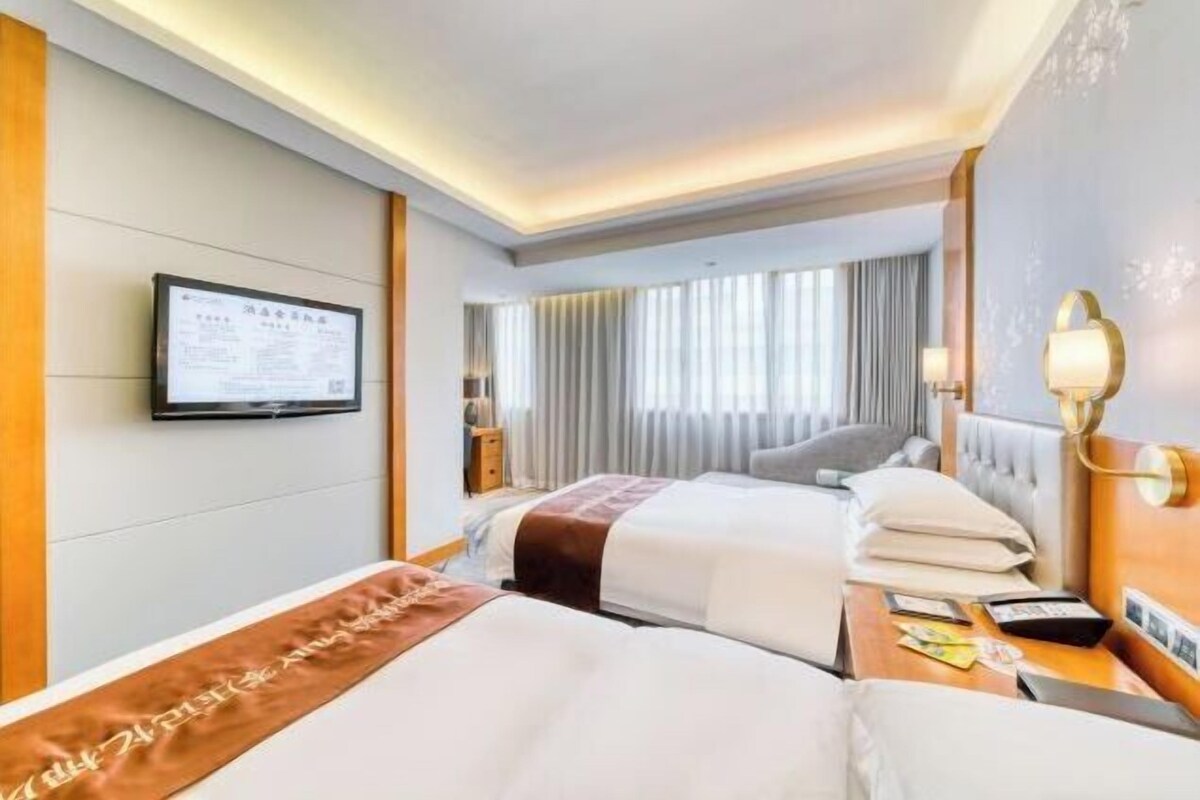 A hotel room with two beds, a television mounted on the wall, and a window with curtains.