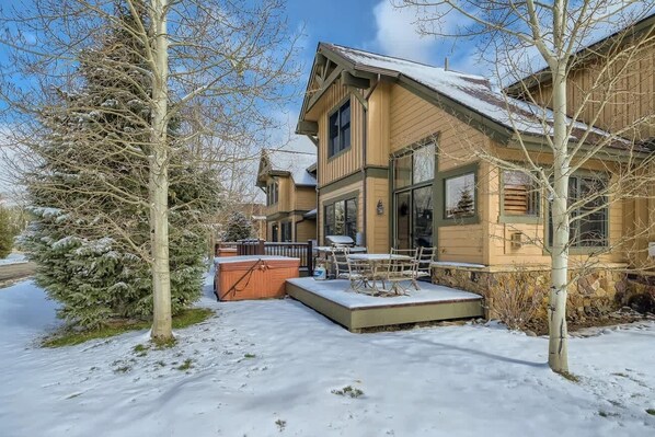 Une maison à deux étages avec une terrasse enneigée et un jacuzzi.