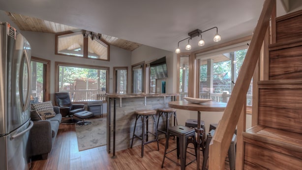 A spacious kitchen with wooden flooring, a dining area with stools, a refrigerator, and a TV mounted on the wall. - Perfect Getaway Cabin w/ Nearby Hike/Bike Trails (Breckenridge)
