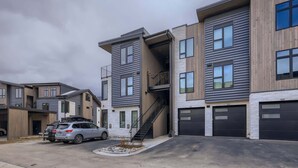 A modern residential building with multiple units, a central staircase, and a parking area with two cars.