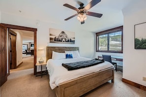 A bedroom with a bed, a ceiling fan, a desk, and a window with a view.