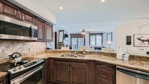 A kitchen with dark wooden cabinets, a granite countertop, stainless steel appliances, and a large window. - Best Mtn View-Ski In/Ski Out & Gondola to Downtown (Breckenridge)