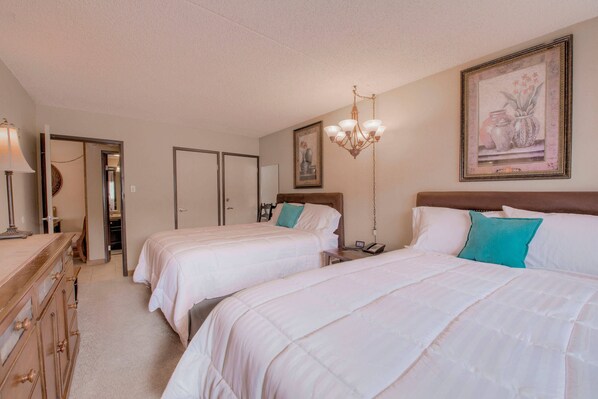 A hotel room with two beds, a dresser, a chandelier, and a framed picture on the wall.