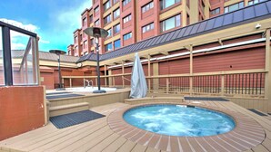 A hot tub on a wooden deck with a view of a red building in the background. - Tons of Amenities! | Ski In Ski Out! (Breckenridge)