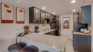 A kitchen with a granite countertop, dark cabinets, a refrigerator, a microwave, and a sink. There are two bar stools at the counter. - Tons of Amenities! | Ski In Ski Out! (Breckenridge)