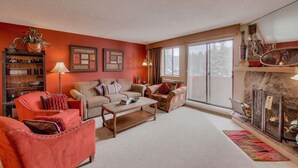 A cozy living room with a fireplace, a sofa, a coffee table, and a bookshelf. - Tons of Amenities! | Ski In Ski Out! (Breckenridge)