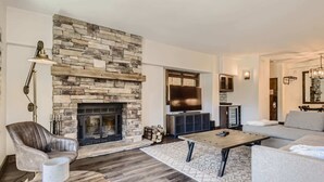 A modern living room with a stone fireplace, a flat-screen TV, a leather armchair, a coffee table, and a sofa.
