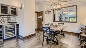 A modern kitchen with a dining area, featuring a large wooden table, chairs, and a chandelier.