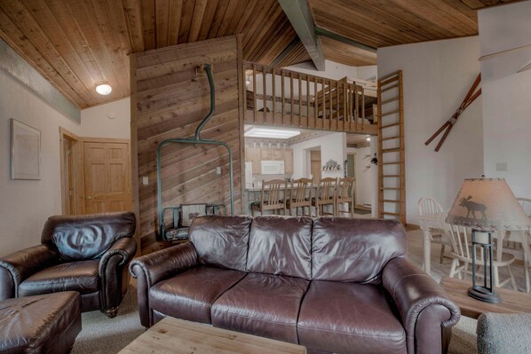 Una sala de estar con un sofá de cuero marrón, una silla de madera, una mesa de madera y una lámpara.