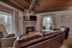 Ein Wohnzimmer mit Kamin aus Stein, einem Ledersofa und einem darüber montierten Fernseher.