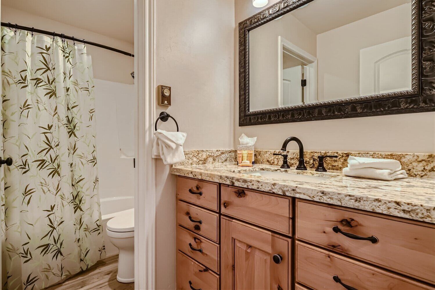 Une salle de bain comprenant des toilettes, un lavabo avec un plan de travail en marbre, des meubles en bois, un porte-serviettes et un grand miroir.