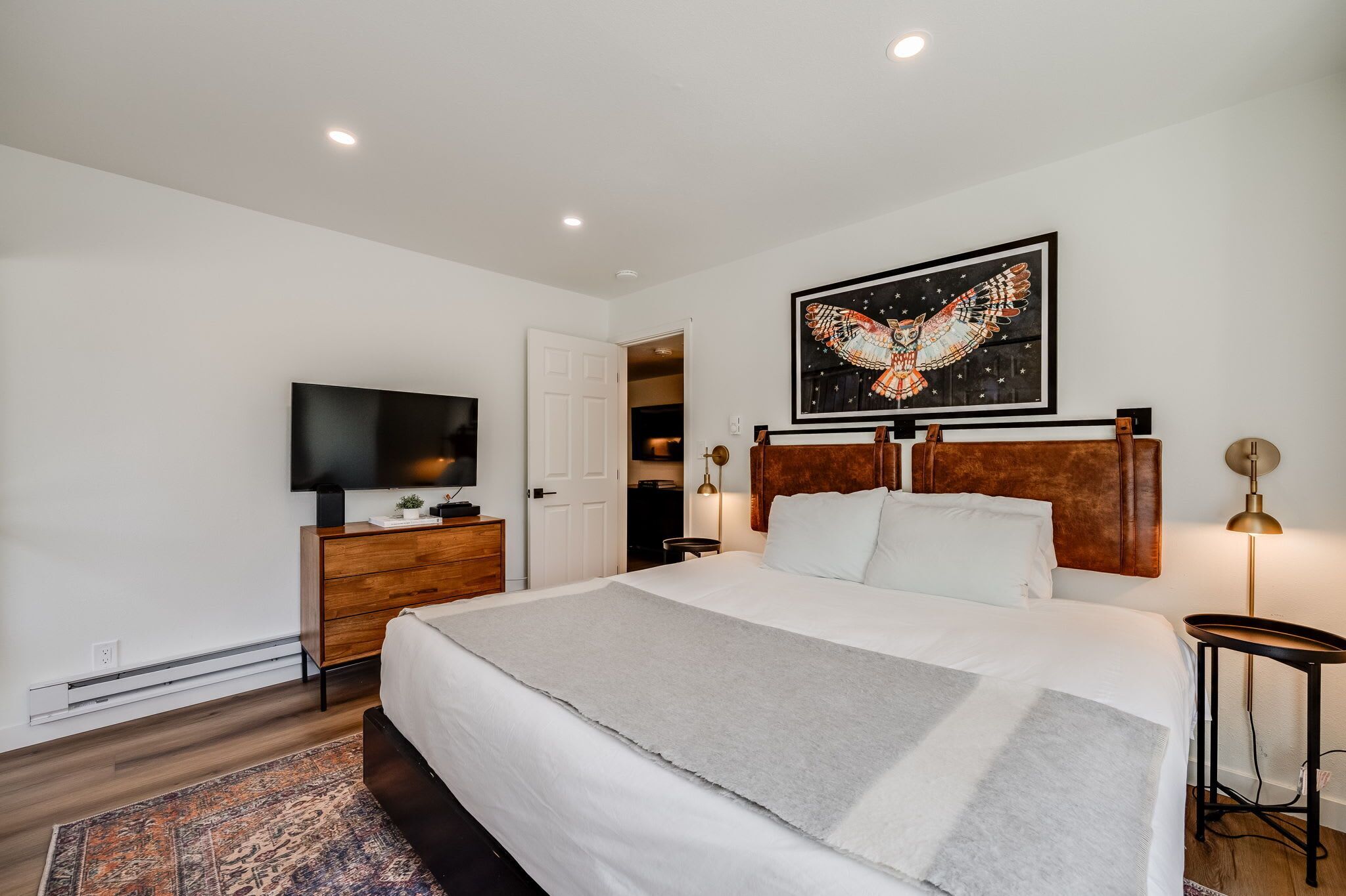 Une chambre à coucher moderne avec un grand lit, une télévision, une commode en bois et un tableau représentant une chouette.