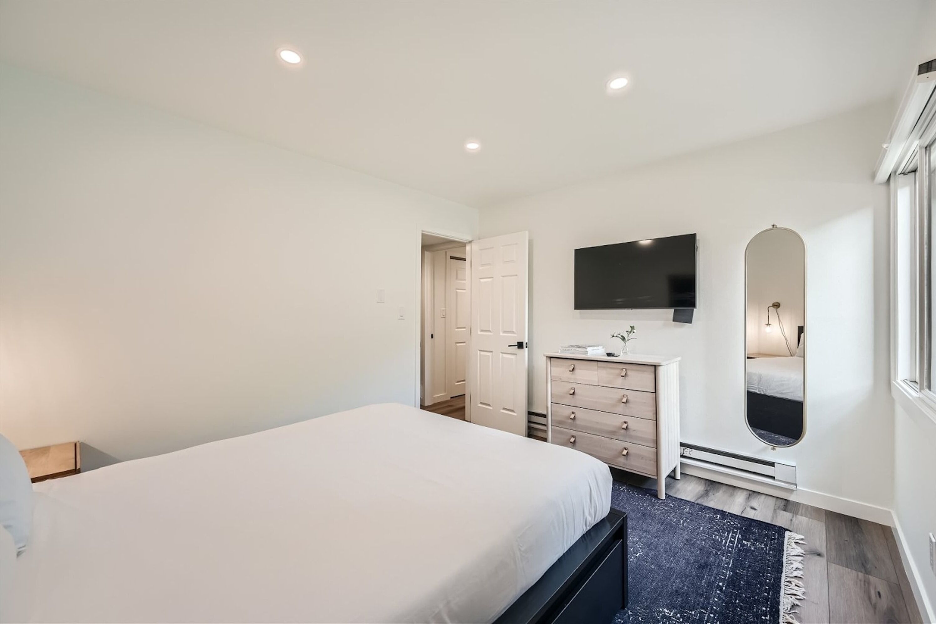 A bedroom with a bed, dresser, TV, and a mirror.