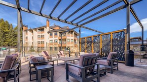 An outdoor patio with seating, a metal pergola, and a view of a multi-story building in the background. - Ski-in/Ski-Out Penthouse Steps from Main Street (Breckenridge)