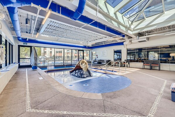 An indoor swimming pool with a slide, a bench, and a view of the outside.