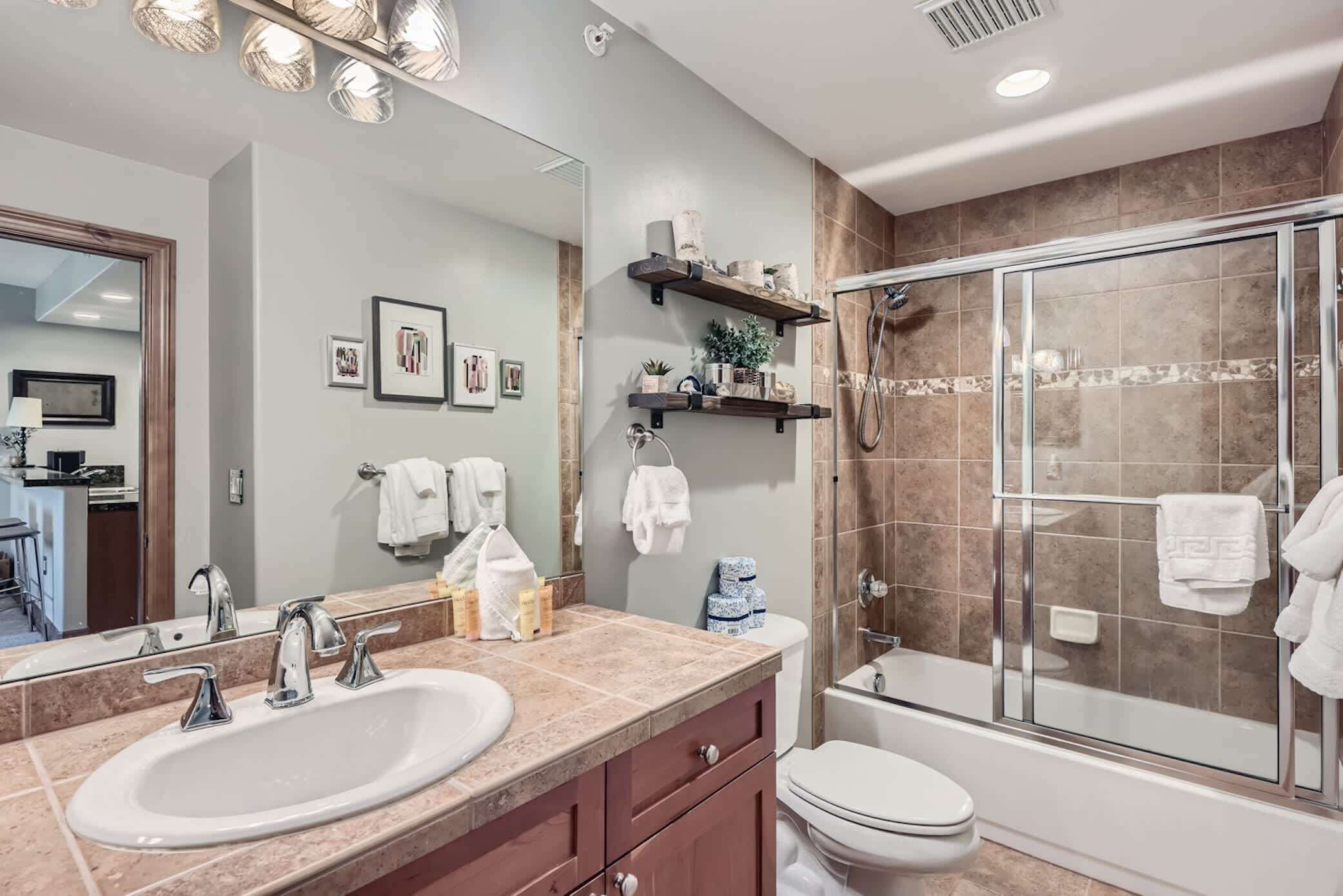 Une salle de bain moderne avec un grand miroir, un lavabo, des toilettes et une douche à parois de verre.