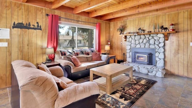 Un intérieur de chalet chaleureux avec une cheminée en pierre, des murs en bois et un coin salon confortable.