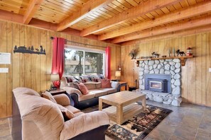 A cozy cabin interior with a stone fireplace, wooden walls, and a comfortable seating area.