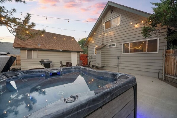 A backyard with a hot tub, string lights, and a house.