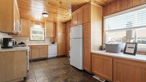 Une cuisine avec des meubles de rangement en bois, un réfrigérateur blanc, une machine à café et une fenêtre avec des stores.