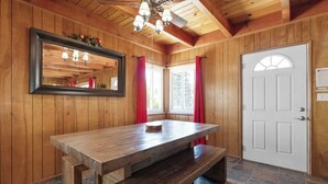 Un intérieur en bois avec une grande table et un banc, une porte blanche et un ventilateur de plafond.