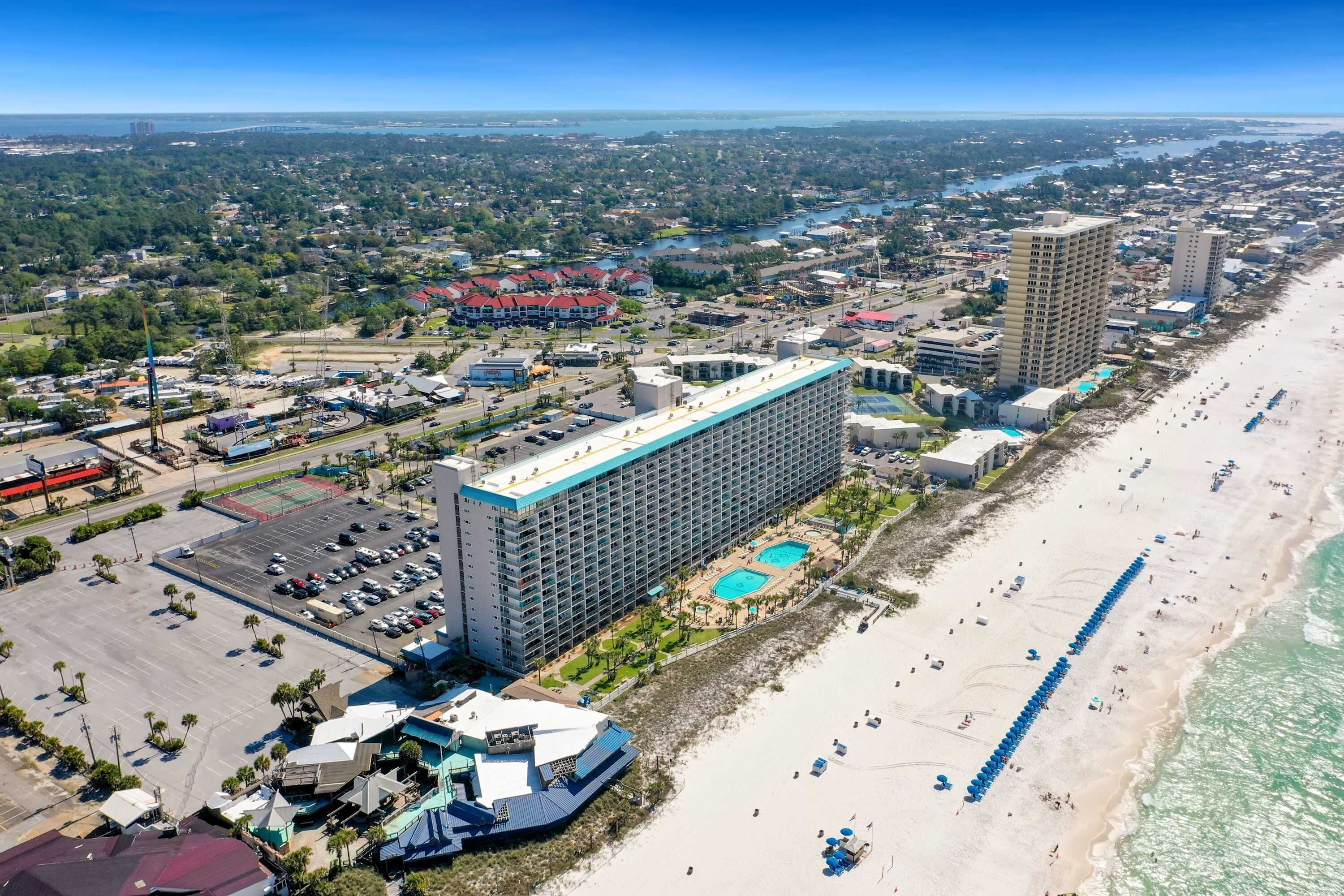 An aerial view of a coastal hotel with multiple buildings, a beach, and a parking lot.