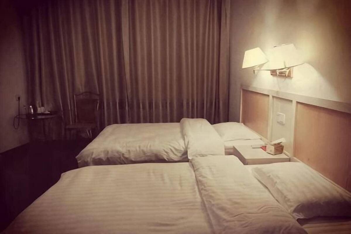 Ein Hotelzimmer mit zwei Betten, einem Nachttisch, einer Lampe und einem Vorhang.