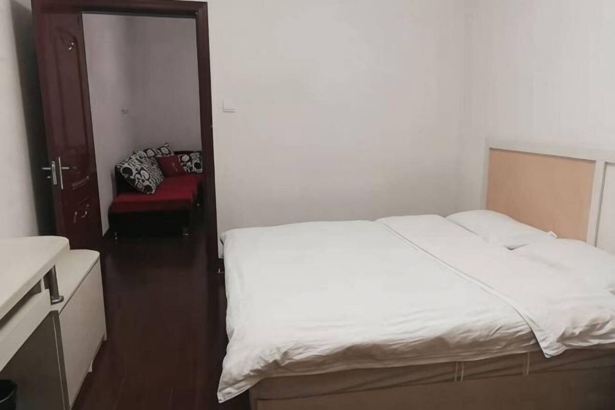 Ein Schlafzimmer mit einem Bett, einem roten Sofa im Hintergrund und einer Tür zu einem anderen Raum.