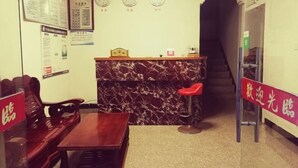 Un espace d’accueil avec un comptoir en marbre, des chaises en bois, une petite table et un tabouret rouge. Il y a des horloges au mur et une enseigne avec des caractères chinois.